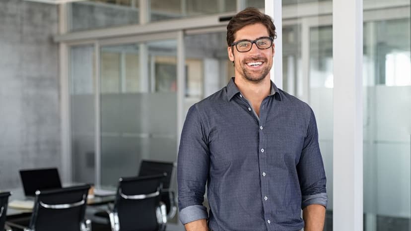 Ein Anwalt mit Brille und lockerem Hemd steht lächelnd in einem modernen Büro