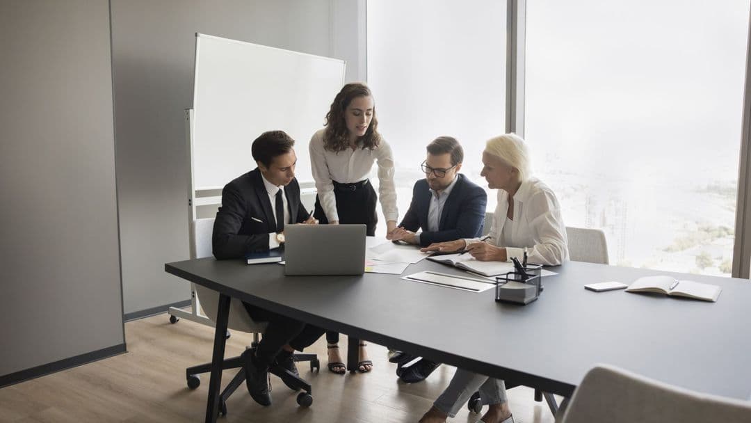 Vier Business-Personen arbeiten gemeinsam an einem Tisch mit Laptop und Dokumenten